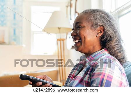 Stock Photography - Mature woman with remote control watching television. Fotosearch