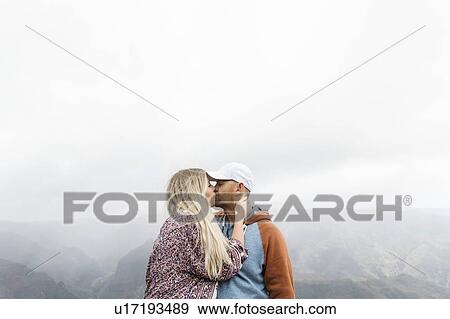 Stock Photo - Mid adult couple kissing by mountains in mist. Fotosearch