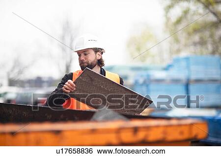 Mid adult male construction worker putting waste into waste skip View Large Photo Image Stock Photograph - Mid adult male construction worker putting waste into waste skip. Fotosearch