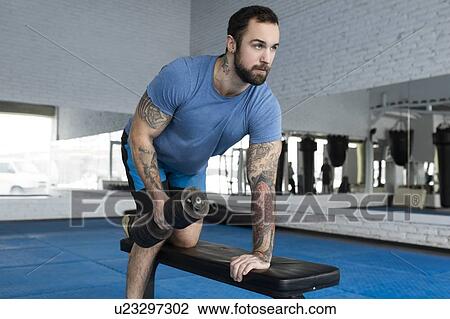 Stock Image - Mid adult man lifting dumbbell in gym. Fotosearch