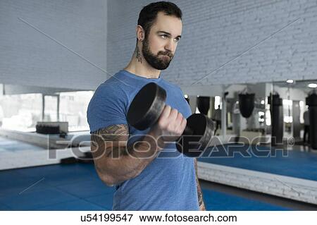 Stock Photo - Mid adult man lifting dumbbell in gym. Fotosearch