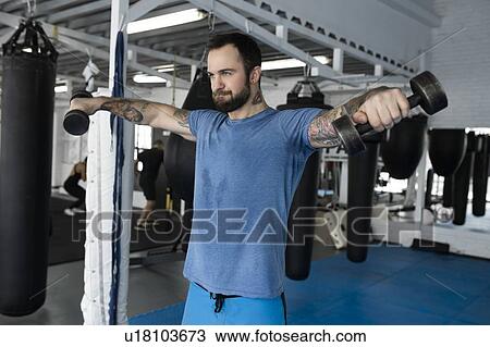 Mid adult man lifting dumbbells in gym View Large Photo Image Stock Image - Mid adult man lifting dumbbells in gym. Fotosearch