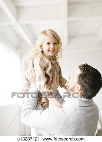 Stock Image - Mid adult man lifting his daughter. Fotosearch