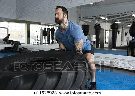 Mid adult man lifting tire in gym View Large Photo Image Stock Image - Mid adult man lifting tire in gym. Fotosearch