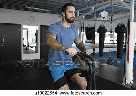 Picture - Mid adult man using exercise machine in gym. Fotosearch