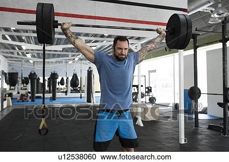 Stock Image - Mid adult man weight lifting in gym. Fotosearch