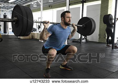 Stock Image - Mid adult man weight lifting in gym. Fotosearch