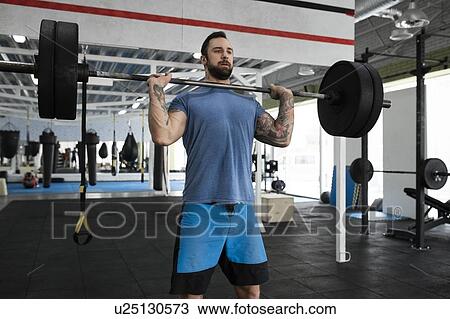 Stock Image - Mid adult man weight lifting in gym. Fotosearch