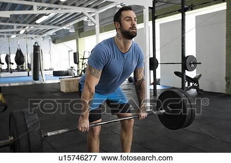 Stock Photo - Mid adult man weight lifting in gym. Fotosearch