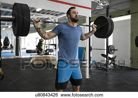 Stock Photograph - Mid adult man weight lifting in gym. Fotosearch