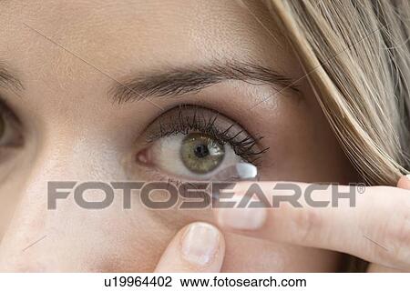 Stock Image - Mid adult woman putting contact lens in eye.. Fotosearch