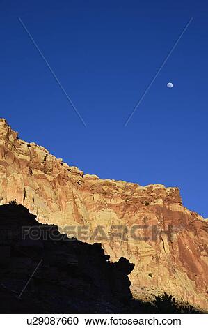 Stock Image - Moon over cliff in shadow in Capitol Reef National Park, USA. Fotosearch