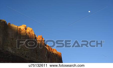 Stock Image - Moon over cliff in shadow in Capitol Reef National Park, USA. Fotosearch