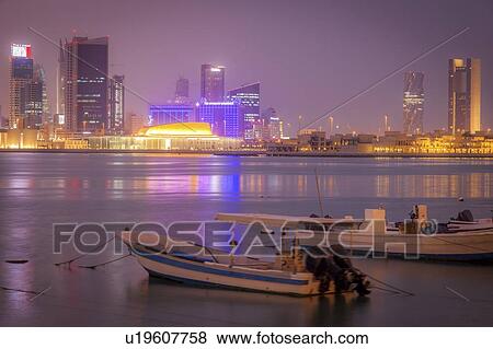 Stock Photo - Moored motorboats by city skyline at night in Manama, Bahrain. Fotosearch