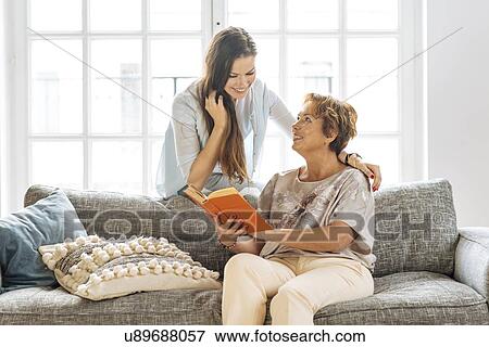 Stock Photo - Mother and adult daughter looking at book on sofa. Fotosearch