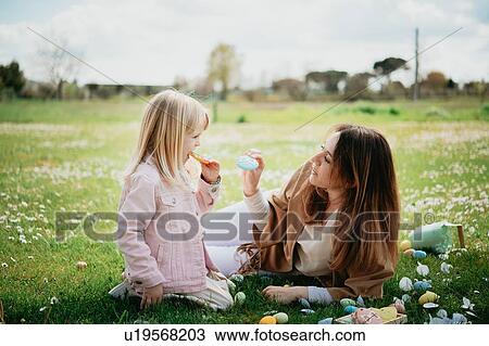 Stock Image - Mother and daughter relaxing in wildflower field after easter egg hunt, Arezzo, Tuscany, Italy. Fotosearch
