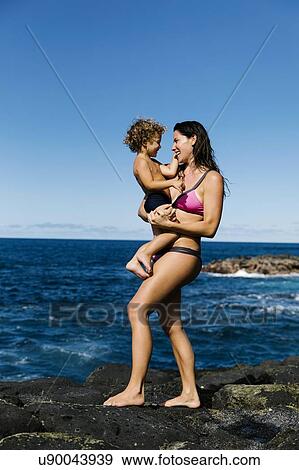 Stock Photo - Mother carrying her son on rocks by sea. Fotosearch