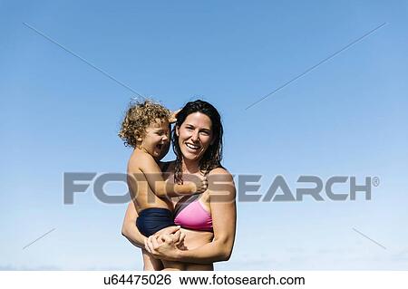 Stock Photograph - Mother carrying her son wearing swimwear. Fotosearch