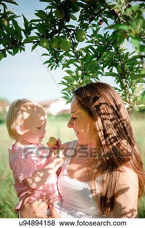 Stock Photo - Mother gazing at toddler daughter under fruit tree, Arezzo, Tuscany, Italy. Fotosearch