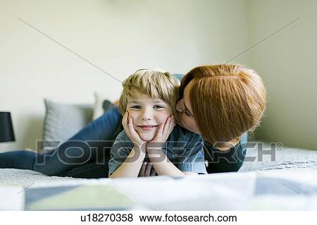 Mother kissing her son's cheek on bed View Large Photo Image Stock Photo - Mother kissing her son's cheek on bed. Fotosearch