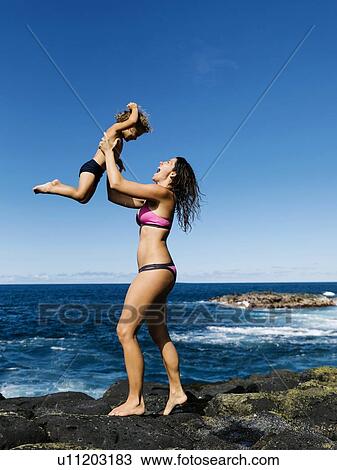 Mother lifting her son on rocks by sea View Large Photo Image Stock Image - Mother lifting her son on rocks by sea. Fotosearch