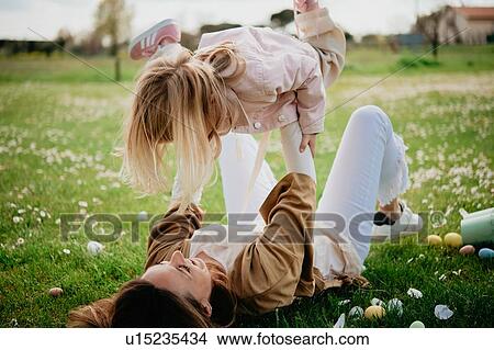 Picture - Mother lying on back holding up daughter in wildflower field after easter egg hunt, Arezzo, Tuscany, Italy. Fotosearch