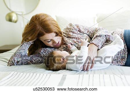 Stock Image - Mother lying on bed with her newborn son. Fotosearch