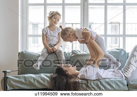 Stock Photo - Mother playing with her daughters on sofa. Fotosearch