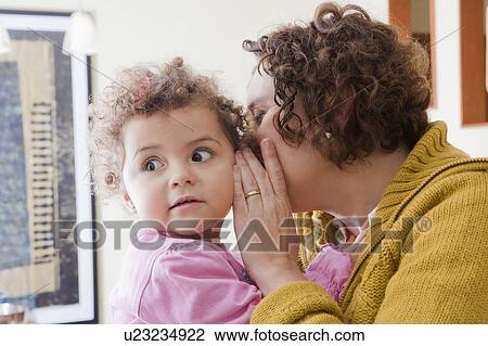 Stock Image - Mother whispering into her daughter's ear. Fotosearch
