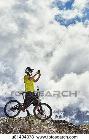 Stock Photo - Mountain biker taking photo, Saas-Fee, Valais, Switzerland. Fotosearch