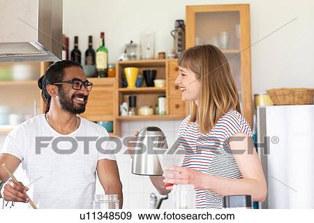 Stock Photo - Multi-ethnic couple talking and cooking in kitchen. Fotosearch