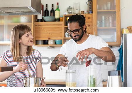 Stock Photography - Multi-ethnic couple talking and cooking in kitchen. Fotosearch