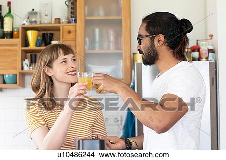 Picture - Multi-ethnic couple toasting with juice in kitchen. Fotosearch
