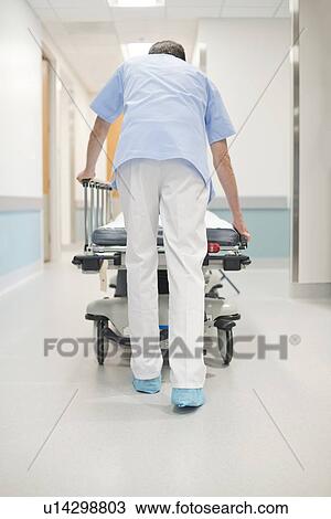 Stock Image - Nurse orderly pushing bed down corridor.. Fotosearch