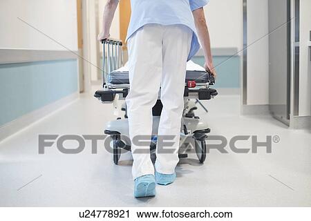 Stock Image - Nurse orderly pushing bed down corridor.. Fotosearch