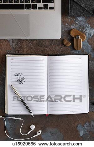 Stock Photograph - Open notebook by laptop with earbuds and USB stick. Fotosearch