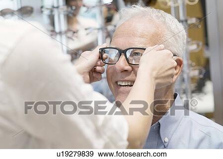 Stock Photo - Optician putting glasses on senior man.. Fotosearch