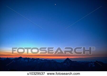 Stock Photo - Orange glow on horizon over mountain range, Saas-Fee, Valais, Switzerland. Fotosearch