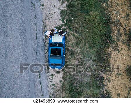 Stock Photo - Overhead view of friends reading route map on car bonnet by roadside. Fotosearch