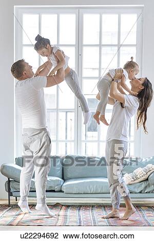 Stock Image - Parent lifting daughters by window. Fotosearch
