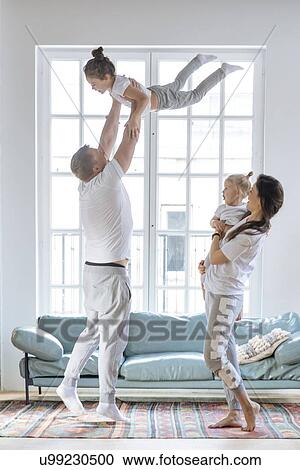 Stock Image - Parent lifting daughters by window. Fotosearch