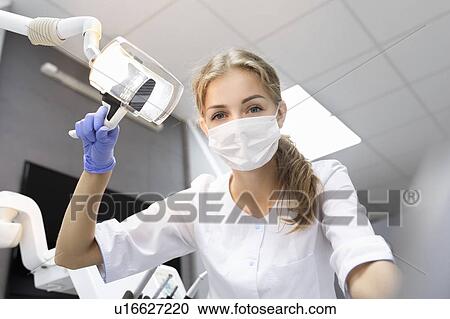 Stock Image - Patient point of view of dental assistant holding light. Fotosearch