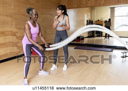Personal trainer encouraging mature woman exercising with ropes in gym View Large Photo Image Stock Photo - Personal trainer encouraging mature woman exercising with ropes in gym. Fotosearch