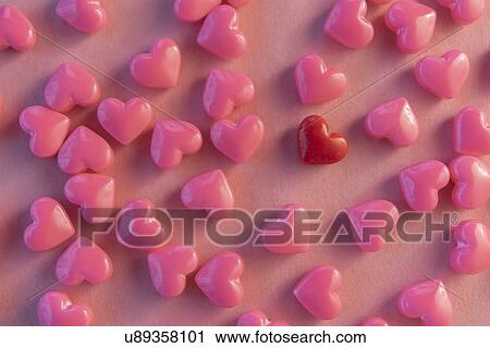Stock Image - Pink and one red heart shaped candy. Fotosearch