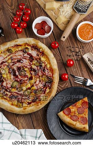 Stock Image - Pizza and ingredients on wooden table. Fotosearch
