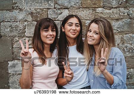 Stock Photo - Portrait of friends gesturing peace sign against stonewall. Fotosearch