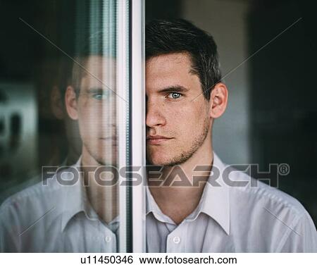 Stock Photograph - Portrait of man looking around glass door. Fotosearch