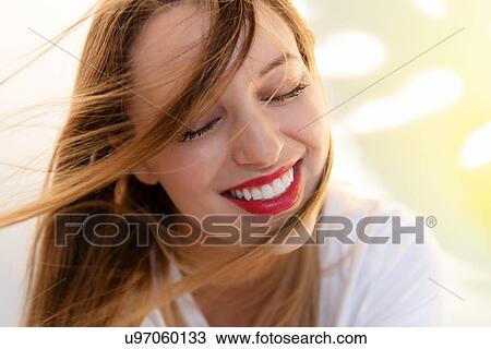 Stock Image - Portrait of windswept young woman wearing red lipstick. Fotosearch