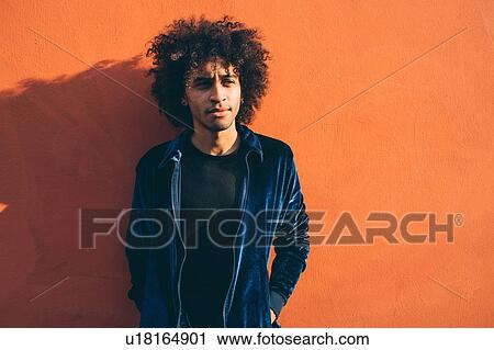Stock Image - Portrait of young man against orange coloured wall. Fotosearch