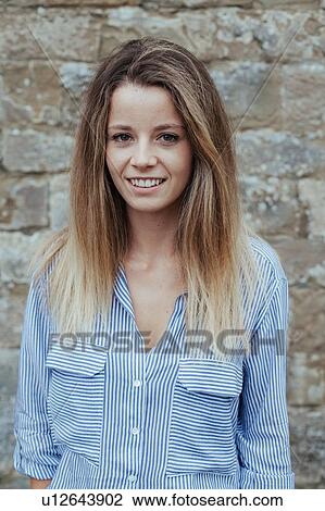 Stock Image - Portrait of young woman against stonewall. Fotosearch
